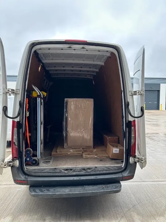 Business moves — wrapped equipment and joinery Business move van with equipment wrapped in protective plastic, Howdens joinery boxes, and a secured hand truck