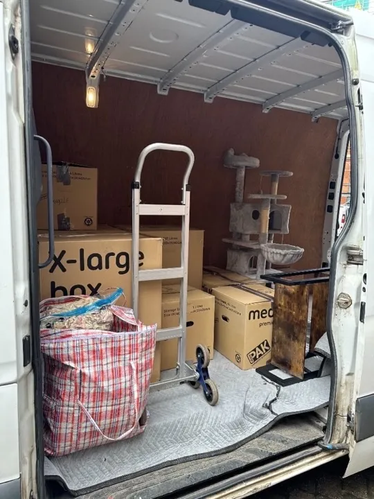 House removals van interior with labelled moving boxes, a cat tree, and a stair-climbing hand truck on protective moving blankets