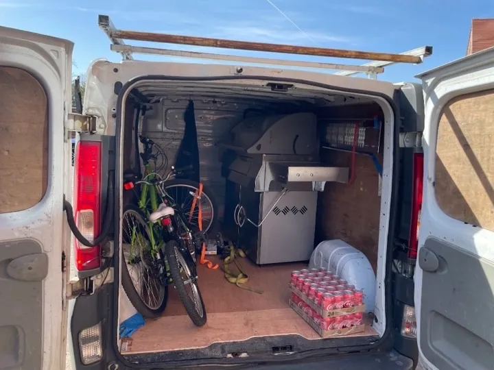 Man and van loaded with bicycles and a stainless steel gas grill secured with tie-down straps for household item collection