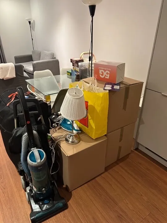 Sealed moving boxes with lamp, iron, vacuum cleaner, and luggage packed and ready for a professional home removals packing service
