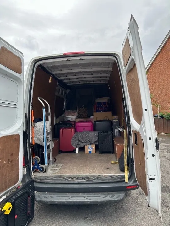 Small move van interior packed with suitcases, cardboard boxes, and a hand truck for a UK studio or apartment relocation